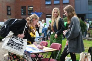 student signing up for a society with 2 students looking on