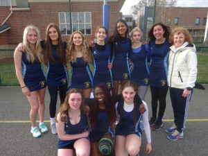 Netball team in their navy sports clothes smiling with the coach Michelle